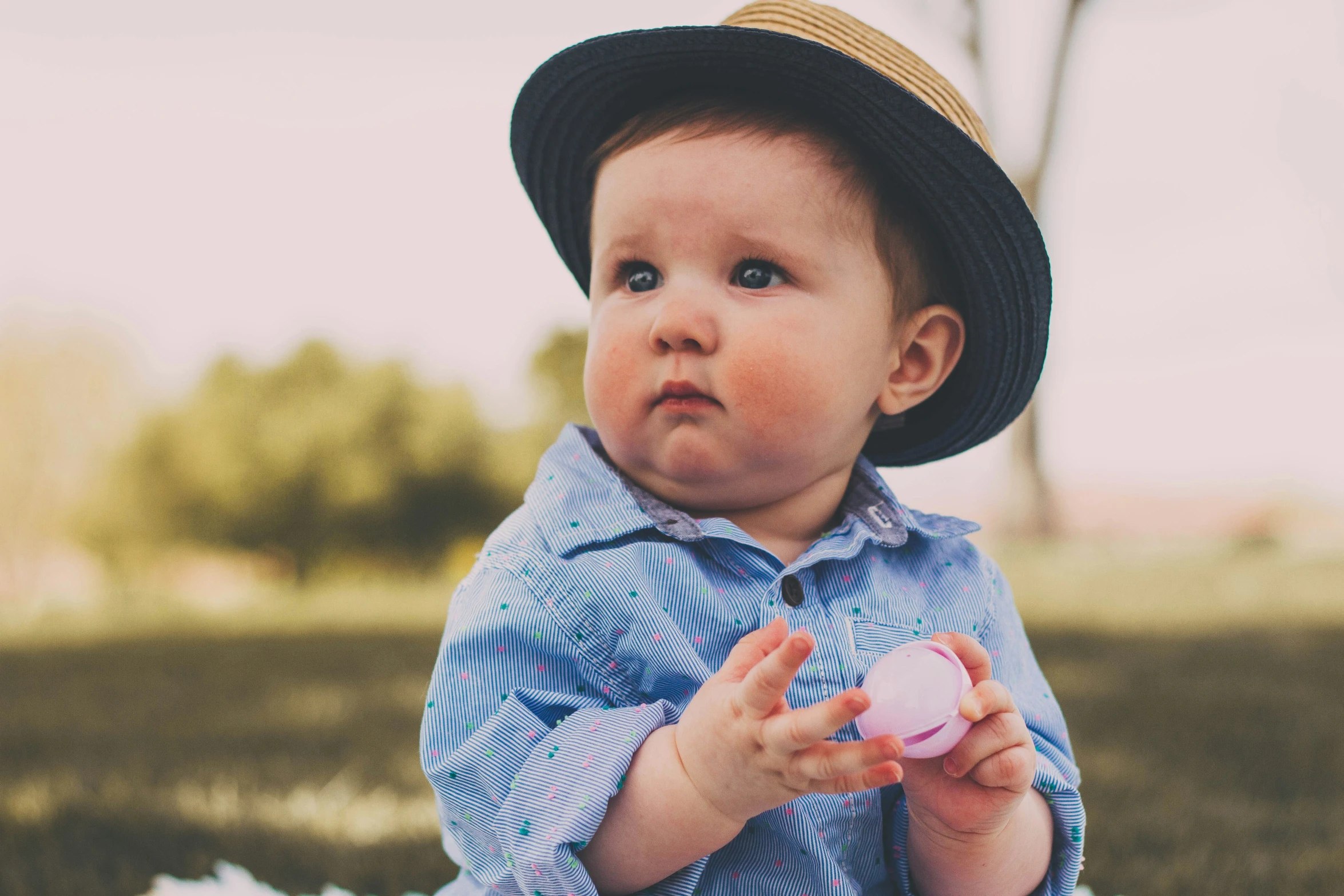 a baby boy wearing a hat while holding a cup