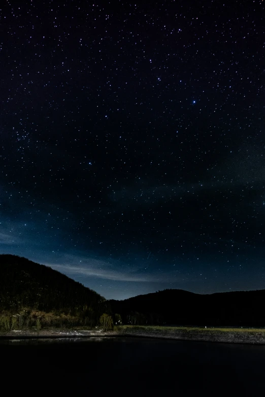 a dark sky filled with stars above mountains and water