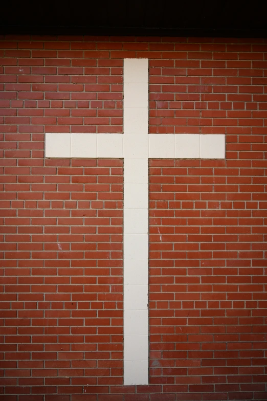 a cross on a wall, painted white and hanging by string