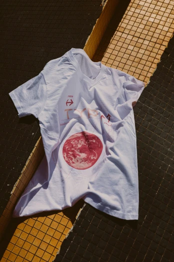 a t - shirt laying on the ground in front of an iron grate