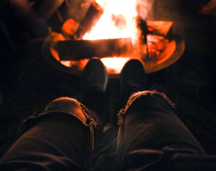 the feet of someone is sitting in front of the campfire