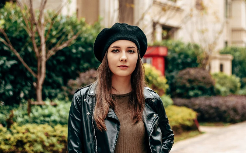 a girl wearing a black leather jacket, brown top and a black hat