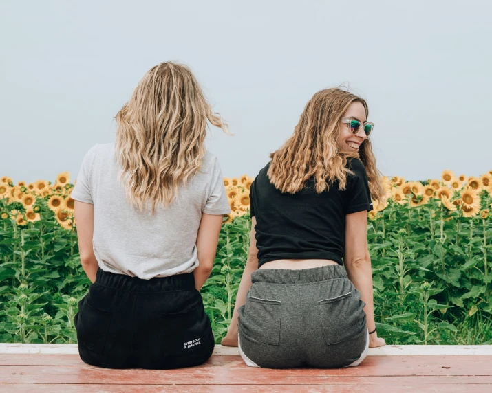 two girls sit on the ground overlooking a field of sunflowers