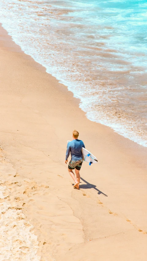 a man walking down a beach carrying a surfboard