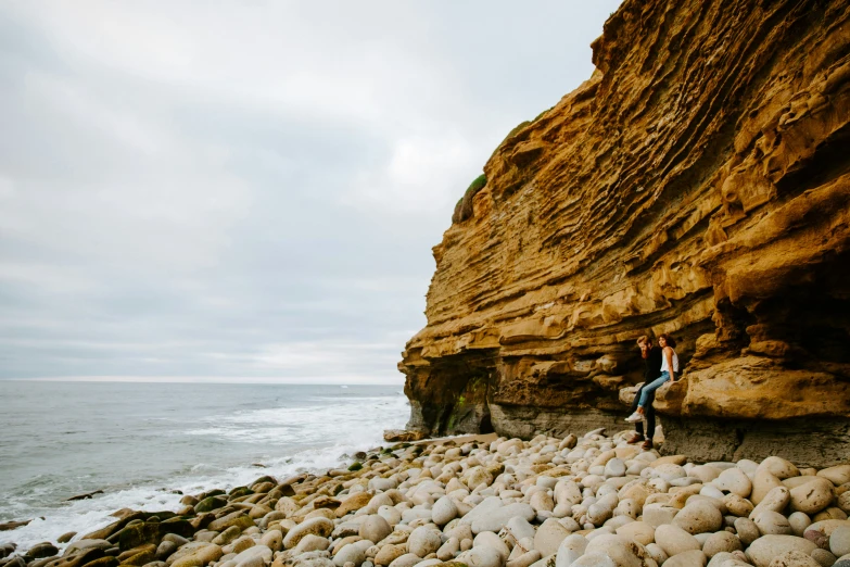 a man sitting on the beach near a big rock