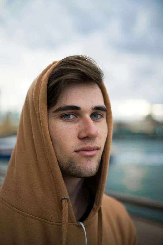 young man standing by the water with hood up on