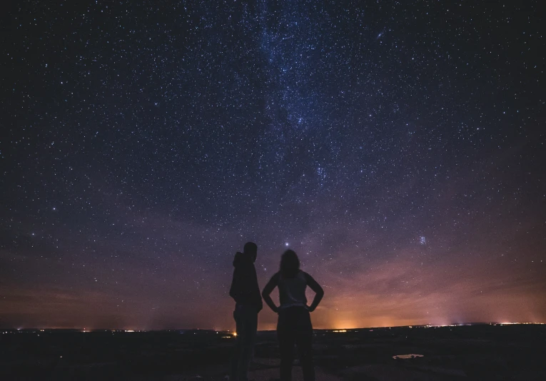 two people stand with their backs facing the stars