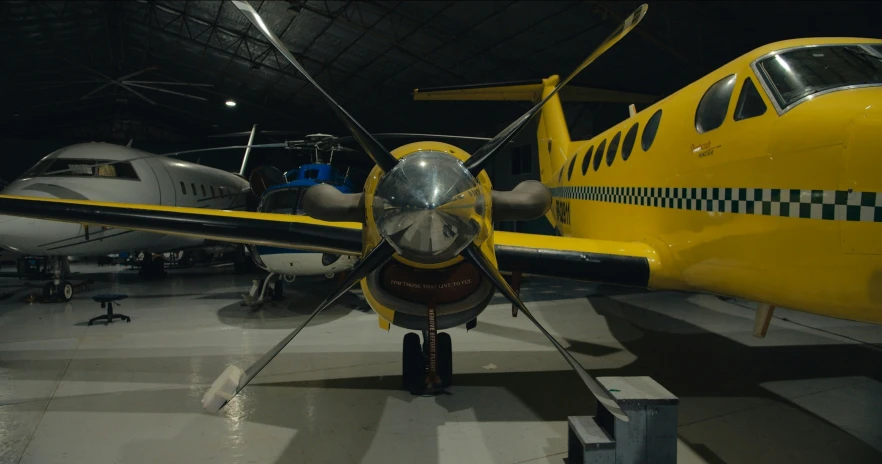 a yellow plane parked inside a hanger with other planes