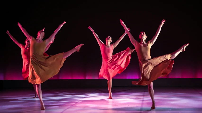 three dancers performing an acrobatic move in a dark background