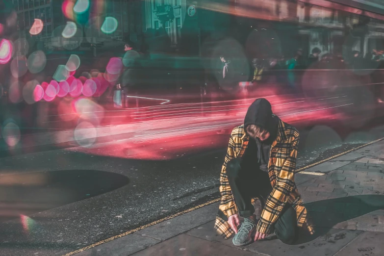 someone sits on the sidewalk in front of a bus stop with their eyes closed