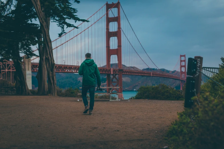 a man in green jacket walking towards the golden gate bridge