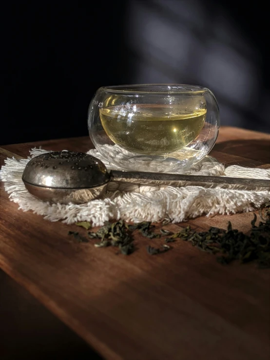 a spoon sits next to a glass of liquid on a cloth with a small tea spoon