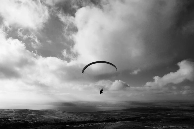 two parachutes are flying over a landscape under cloudy skies