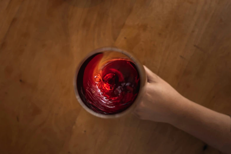 a person holds a wine glass with a red substance