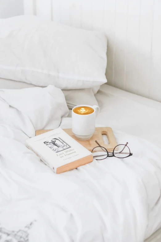 a cup of coffee and glasses on top of an unmade bed