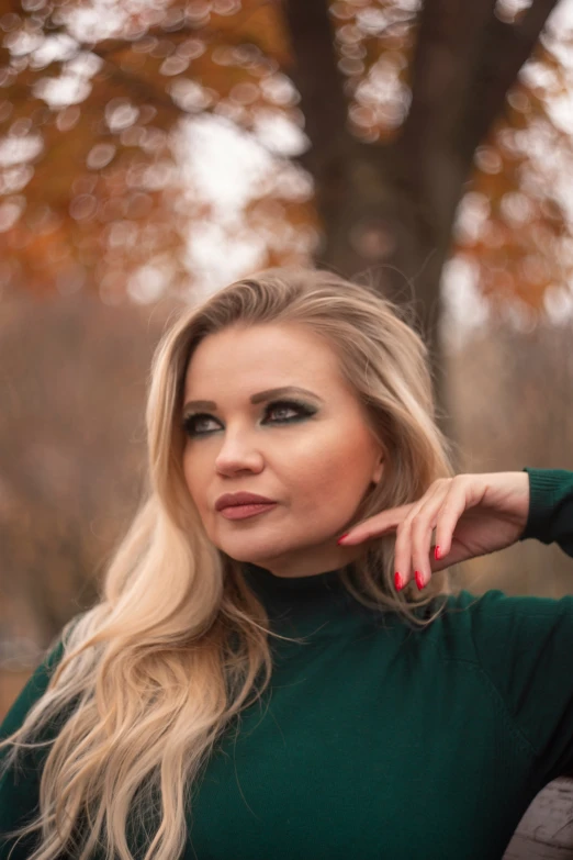 a blonde haired woman with green sweater and nails on posing