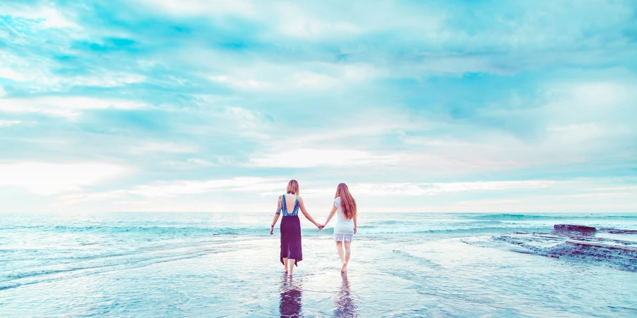 two women walk along the beach on the shore line