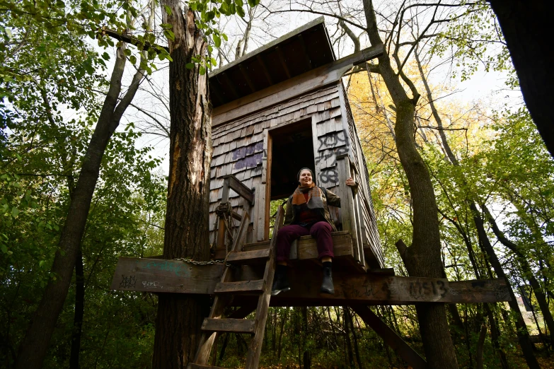 a woman in black shirt sitting on a platform next to a tree house
