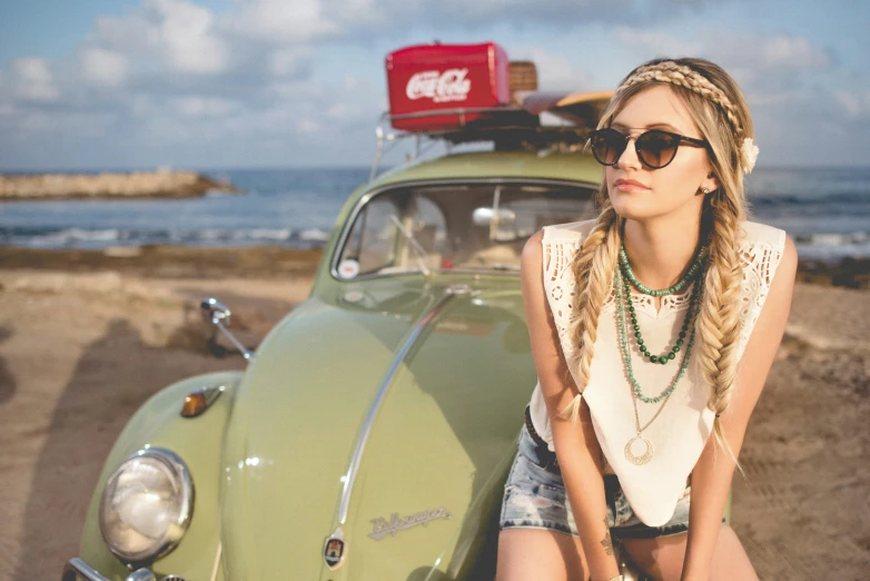 young woman poses next to her car on the beach