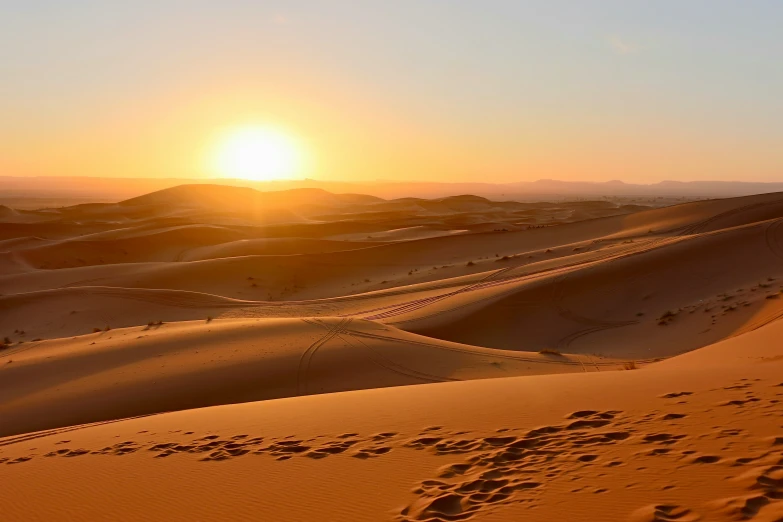 the sun rising over the desert with footprints in the sand