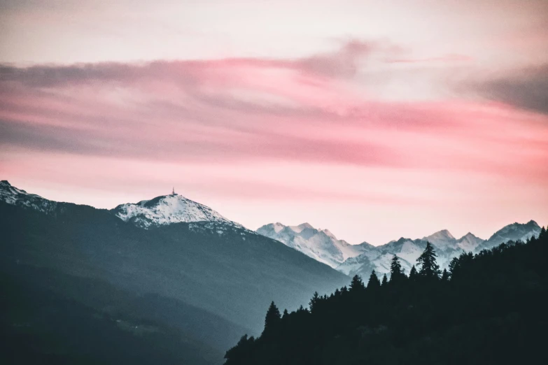 a pink sky over the mountains with a cross on top