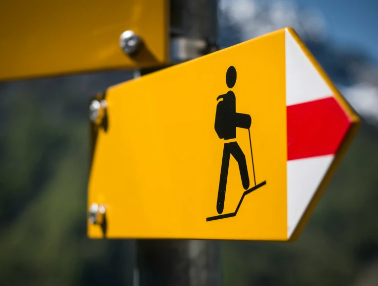 a yellow pedestrian crossing sign hanging from the side of a pole