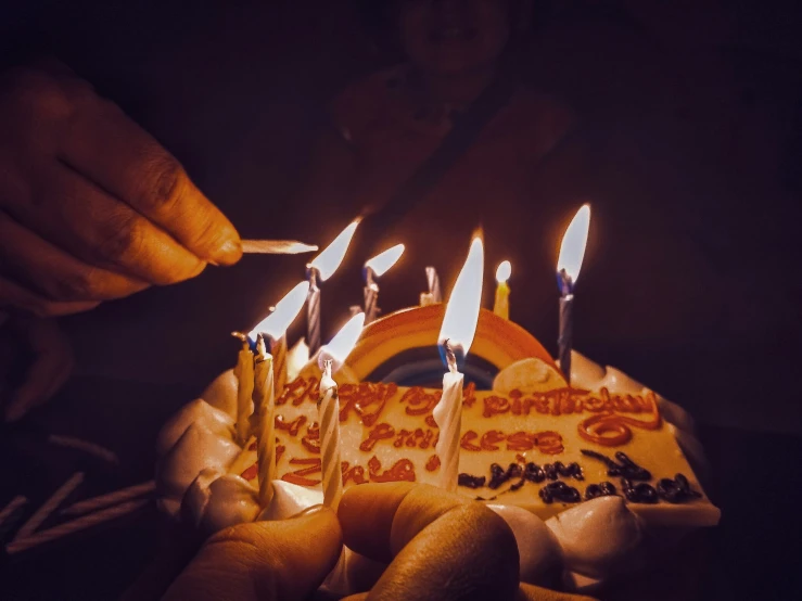a person lighting the candles of a birthday cake