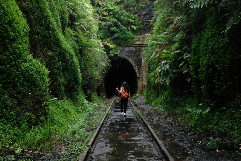 a woman walks down a narrow railway with trees on either side