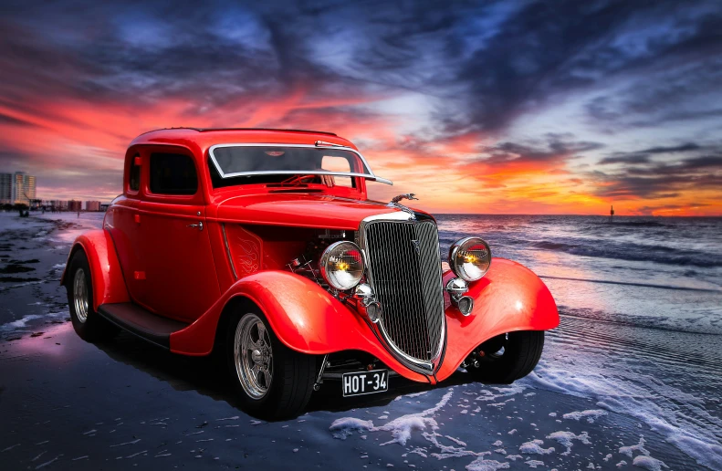 a vintage car parked on the beach with sunset in the background