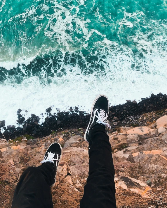 person standing on rocks next to an ocean with a view of their shoes