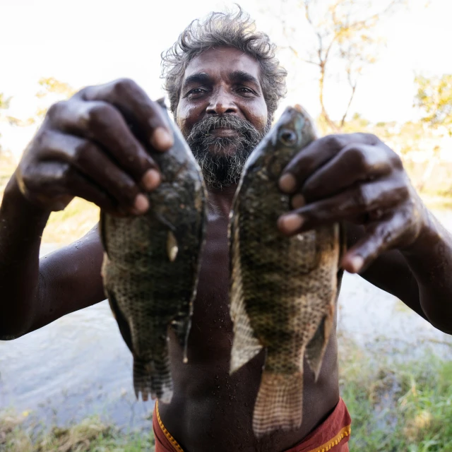 the young man is holding two fish up to his face