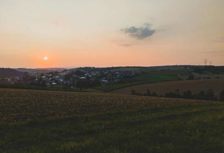 the sun rising over a field and town