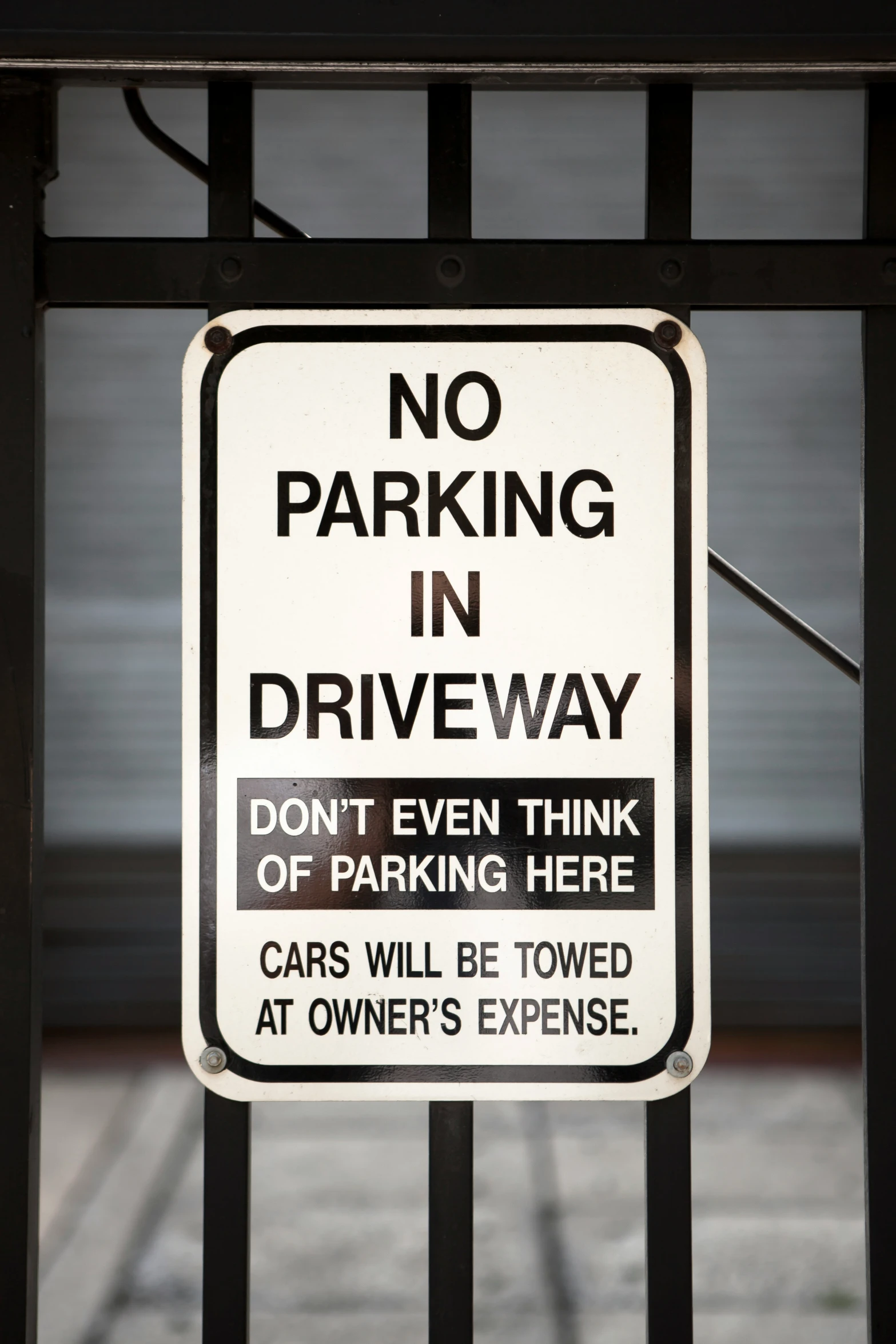 a no parking in driveway sign hanging on a black metal gate