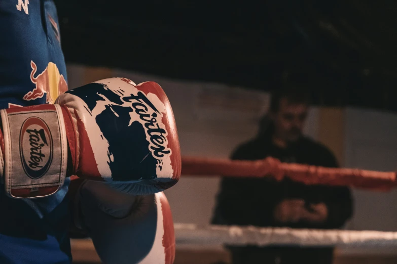 the hand holds a boxing glove while a man stands in the background
