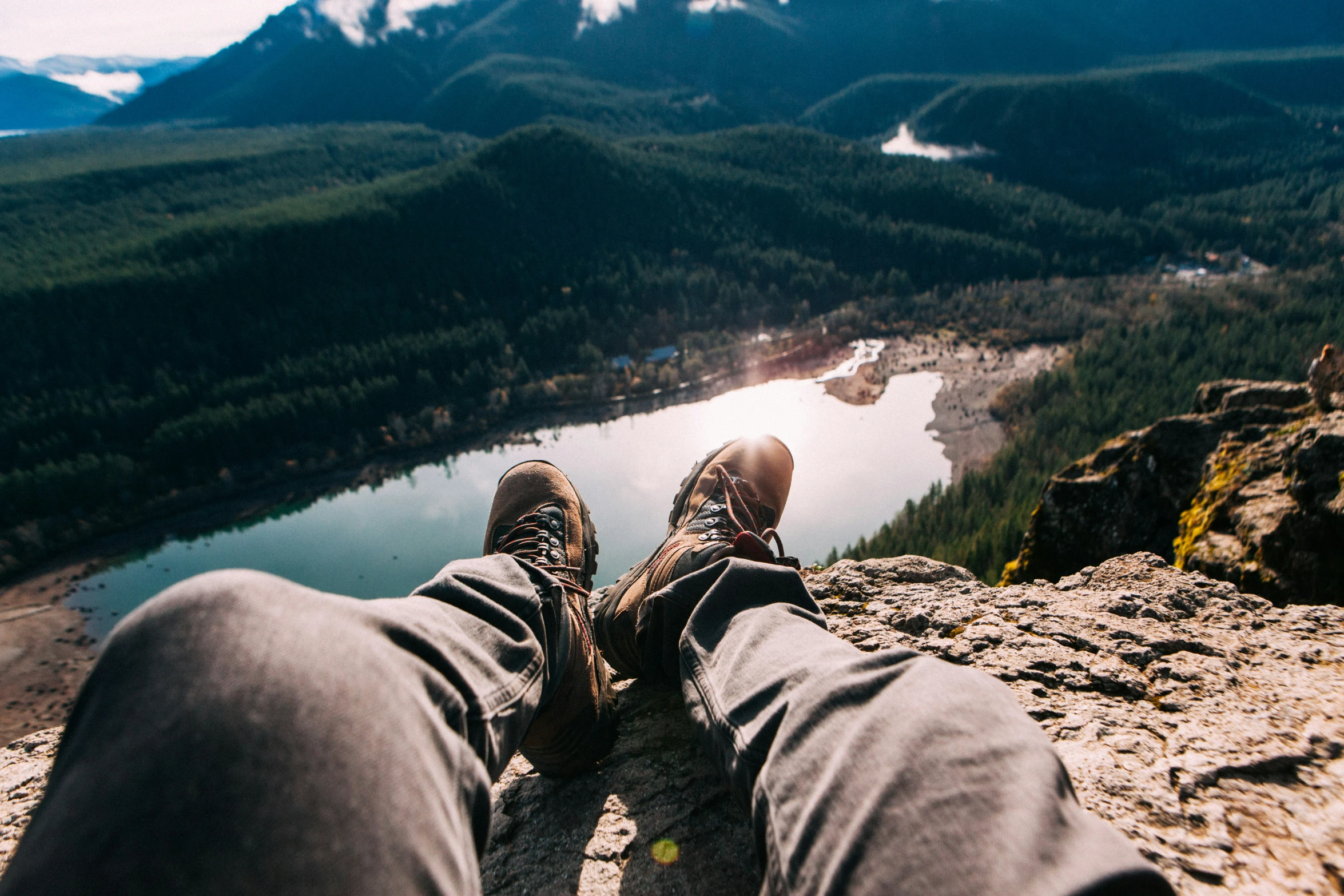 a persons legs resting on top of a mountain next to a lake