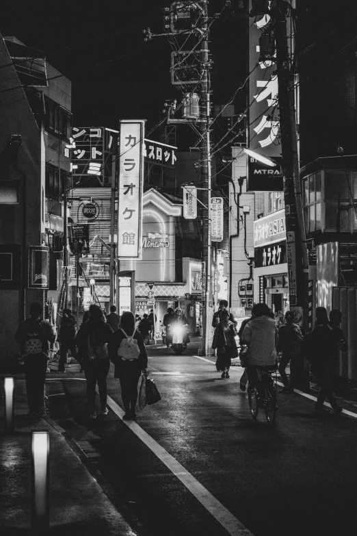 people walking along a street at night with tall buildings