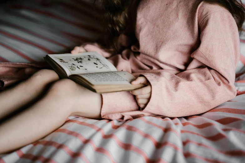 a girl in pink is laying on a bed reading a book