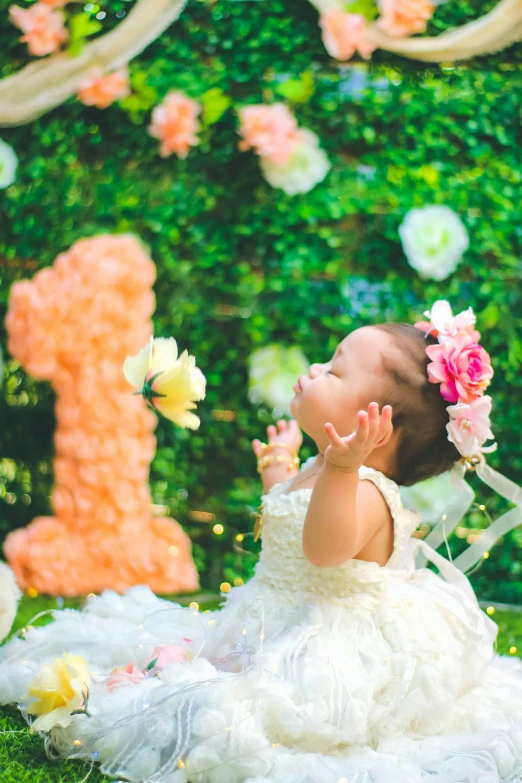 a little baby girl dressed in a white dress and headpiece playing with flowers
