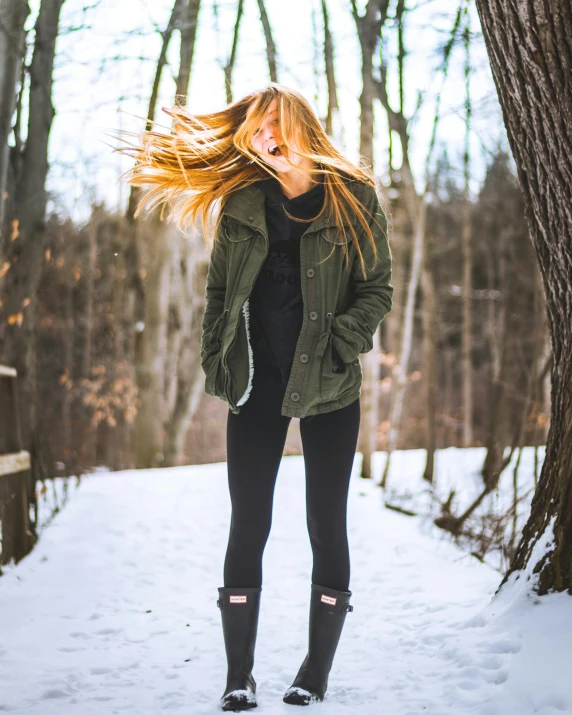 a woman with long hair is standing in the snow by a tree