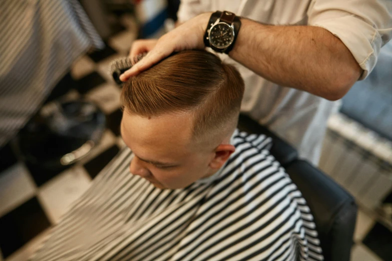 a barber  another barber's hair while sitting in front of a checkered wall