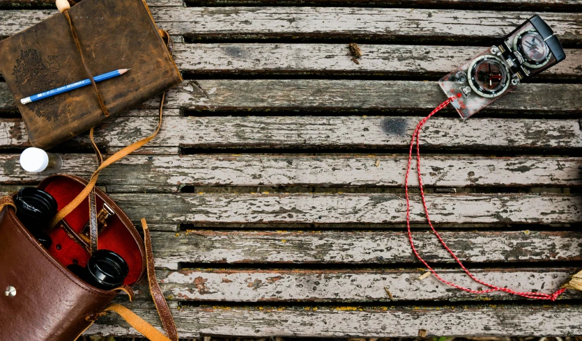 a camera, a bag and a pair of glasses sitting on the back of an old bench