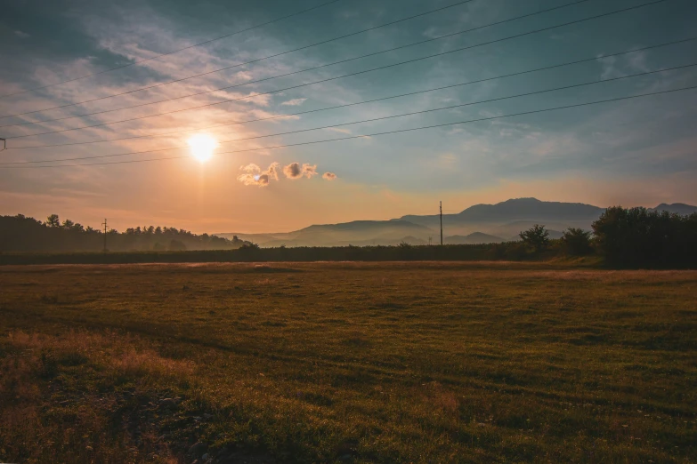 the sun sets over the hills near an empty field