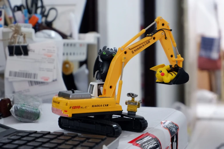 a toy excavator is on the desk next to a computer