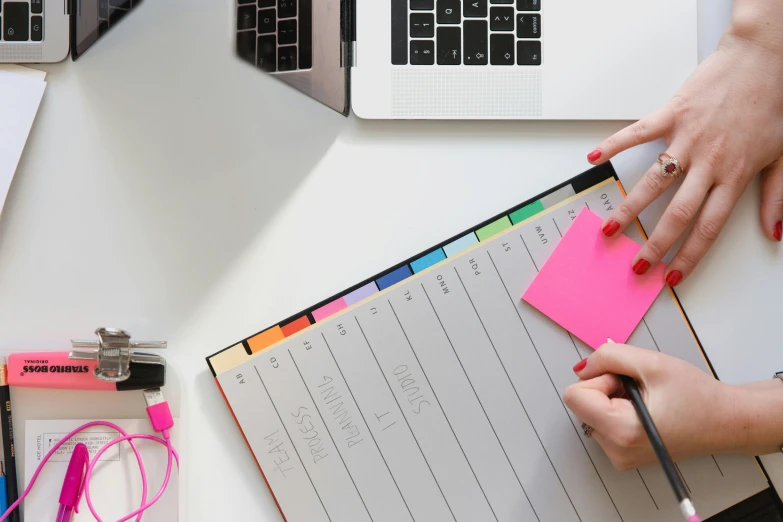 two people writing with notepads next to laptops