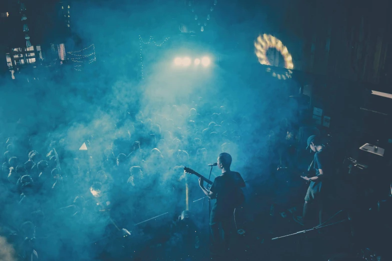 three people playing instruments on stage while light is from a spotlight