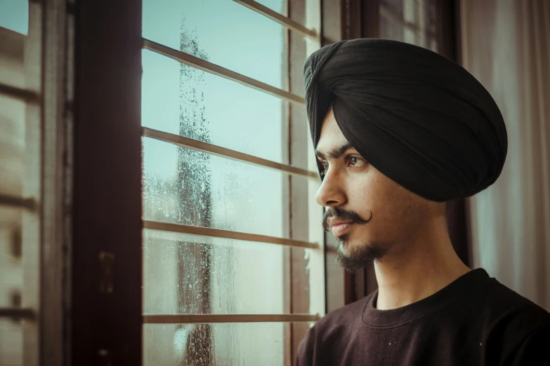 man in turban looking out window in front of a rain soaked window