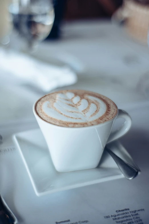 a cappuccino is in a white cup on a saucer on top of a table