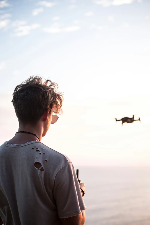 man standing on beach watching two airplanes flying in the sky