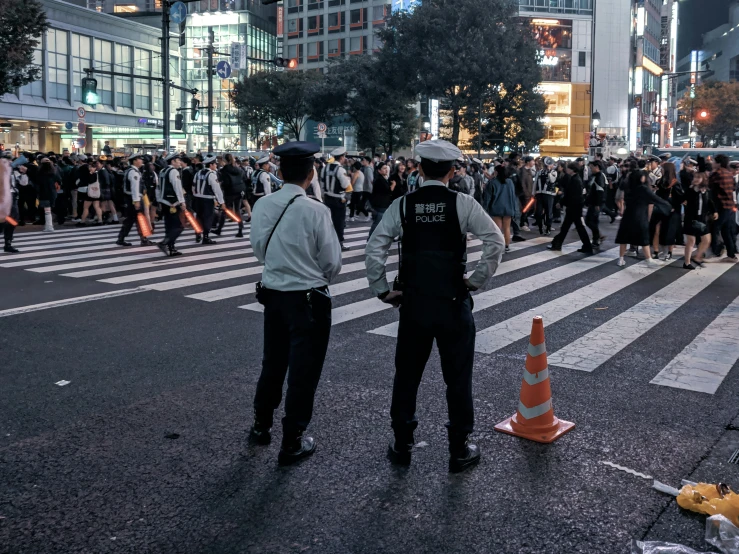 two policemen stand on the street corner in front of a crowd