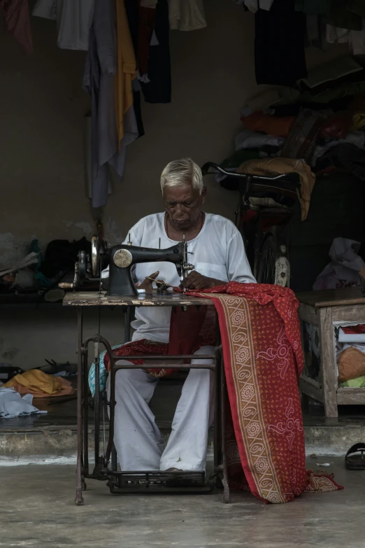 man in white sitting at sewing machine in his home